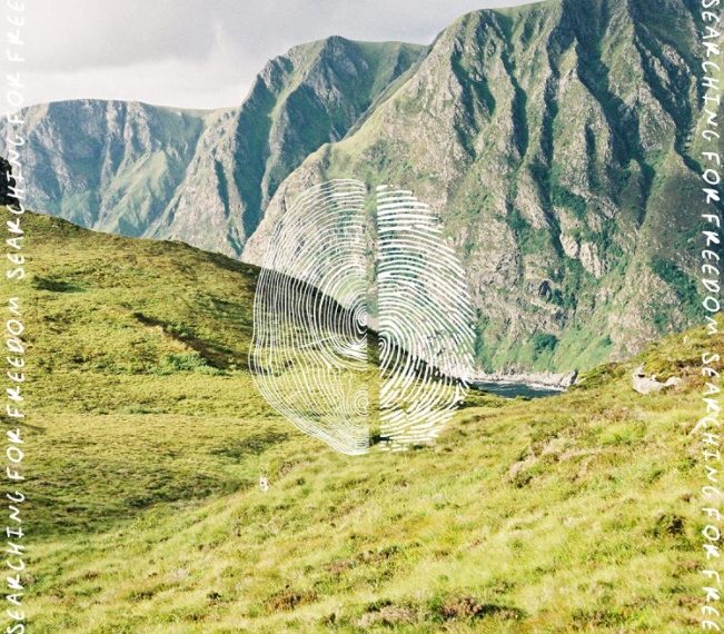 Auf dem Albumcover "Searching For Freedom" von Ziggy Alberts ist ein Bergpanorama zu sehen. Im Vordergrund ist ein grüne Wiese, im Hintergrund sind graue und Berge. In der Mitte des Bildes befindet sich ein weißer Fingerabdruck. An den Rändern steht immer wieder der Albumtitel "Searching For Freedom".