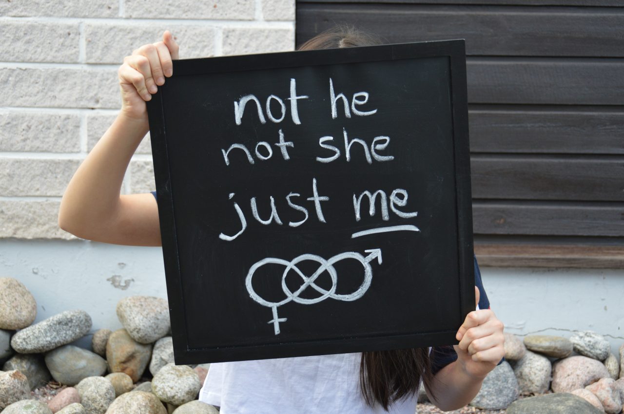 Ein Mädchen hält eine Tafel hoch, auf der "not he, not she, just me" steht.