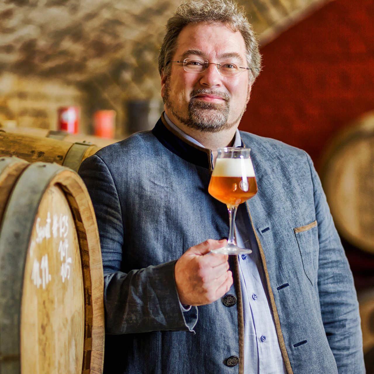 Auf dem Foto ist Markus Raupach mit einem Bier in der Hand vor Bierfässern zu sehen.