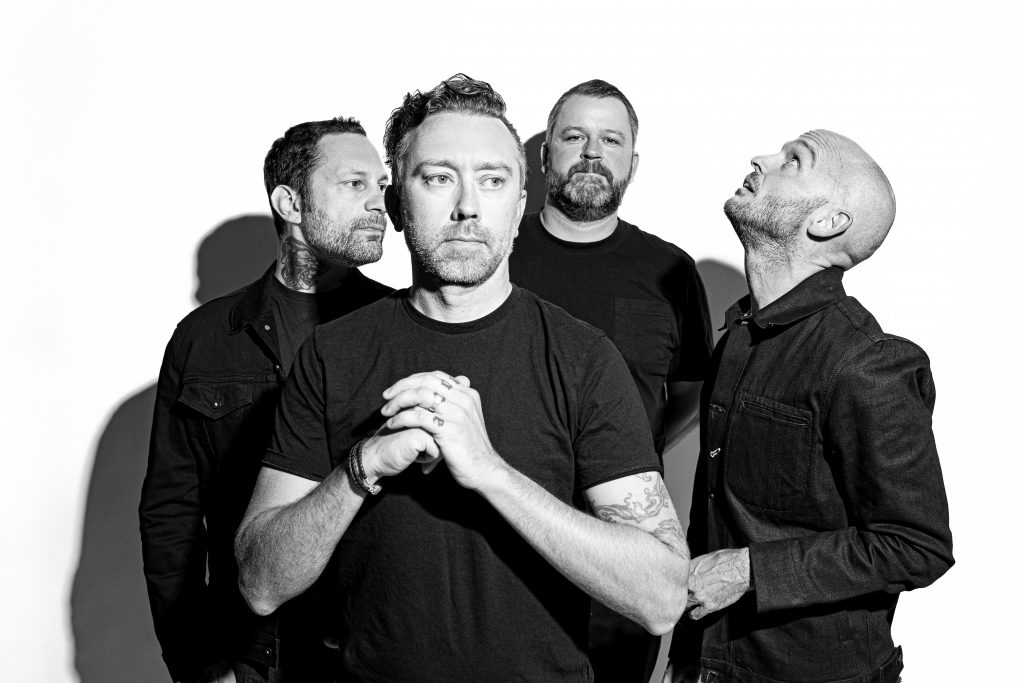 Das ist ein Gruppenfoto von Rise Against in schwarz-weiß.