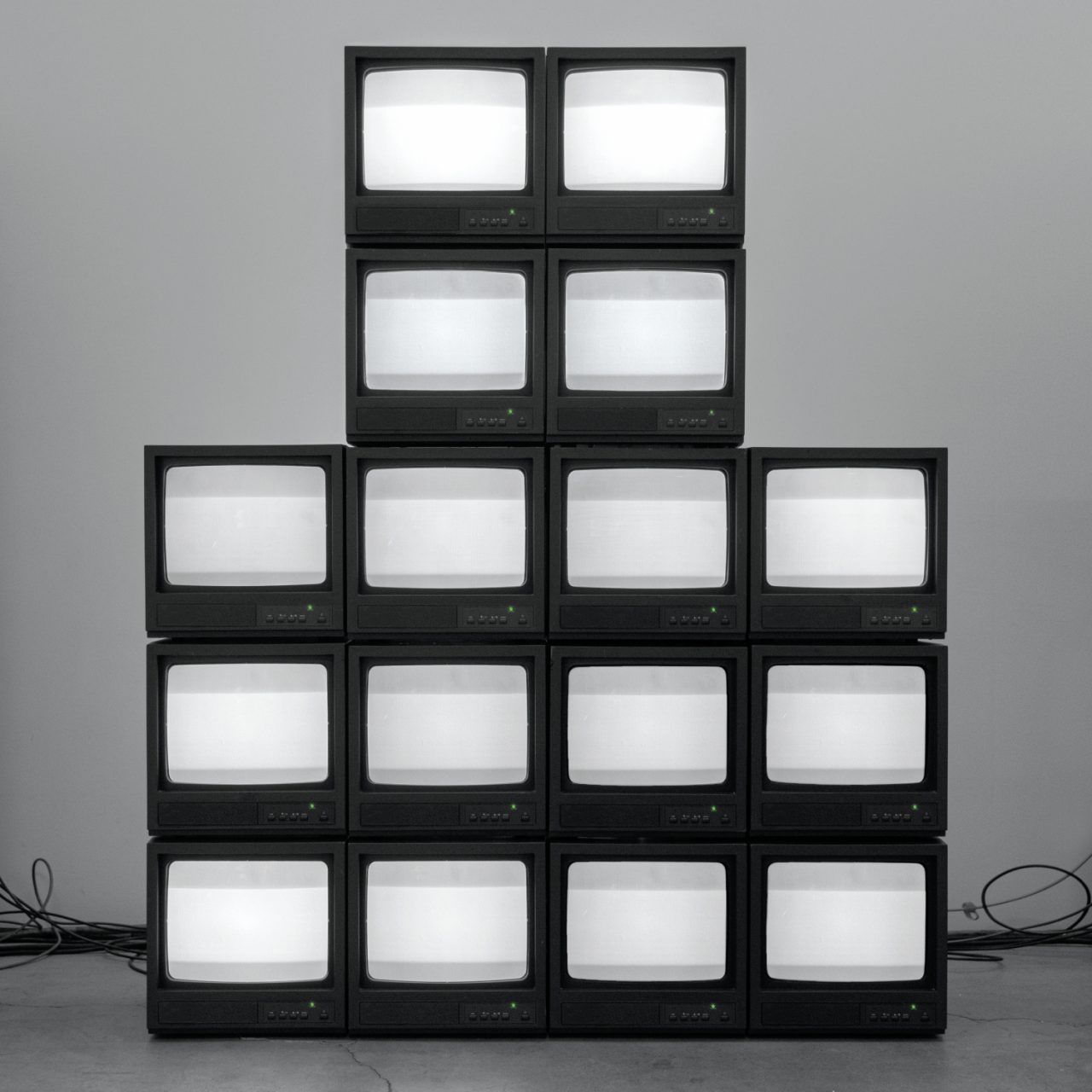 Auf dem Albumcover "Nowhere Generation" von Rise Against sieht man eine Pyramide aus alten Fernsehern vor einer grauen Wand.