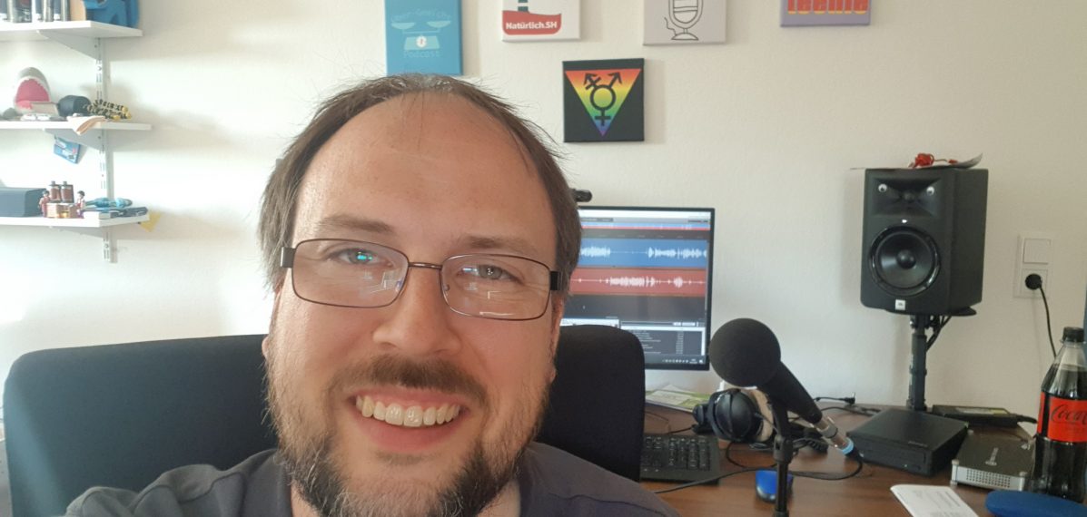 Jörn Schaar hat ein Selfie an seinem Schreibtisch gemacht. Im Hintergrund sieht man einen Computer, Mikrofon und Bilder an der Wand.