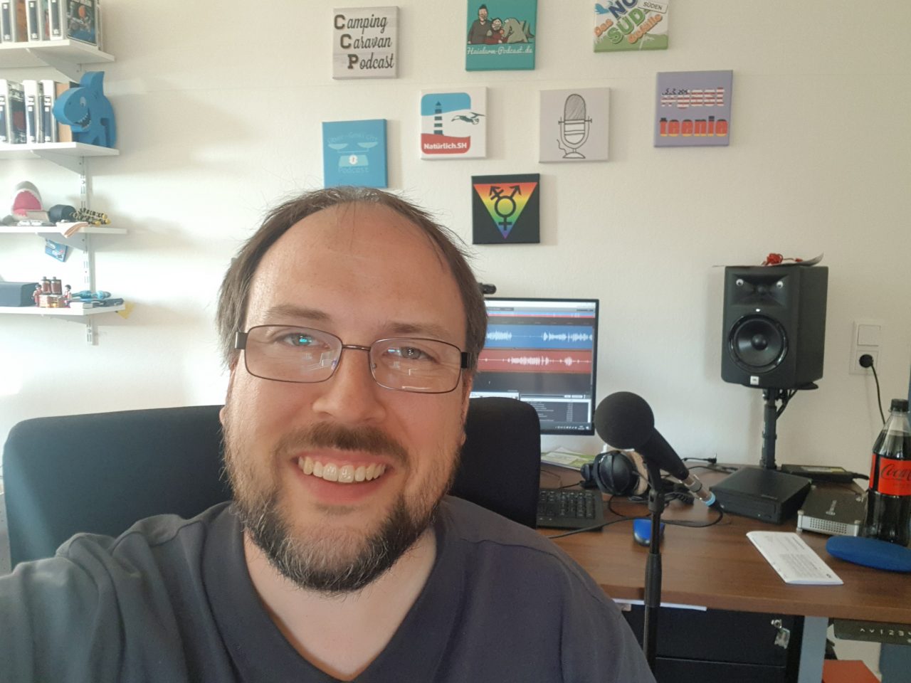 Jörn Schaar hat ein Selfie an seinem Schreibtisch gemacht. Im Hintergrund sieht man einen Computer, Mikrofon und Bilder an der Wand.