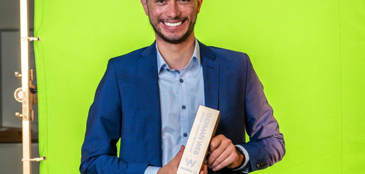 Oliver Winkler steht vor einem Greenscreen mit einem "German Web Award" in der Hand.