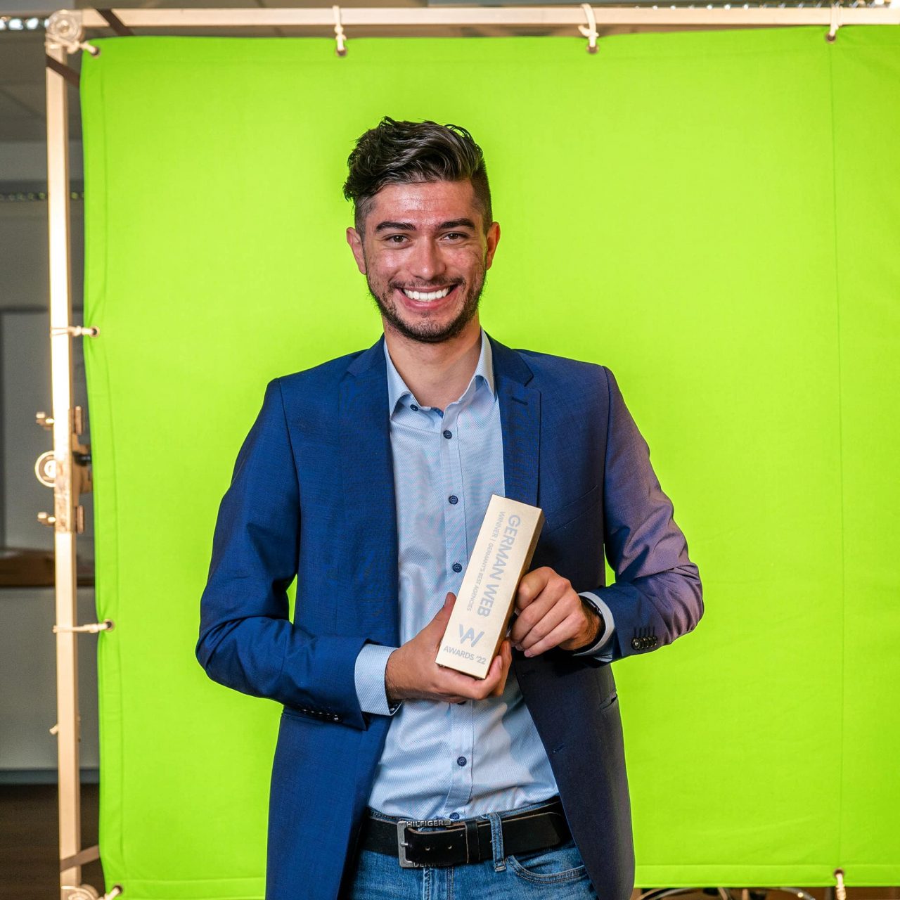 Oliver Winkler steht vor einem Greenscreen mit einem "German Web Award" in der Hand.