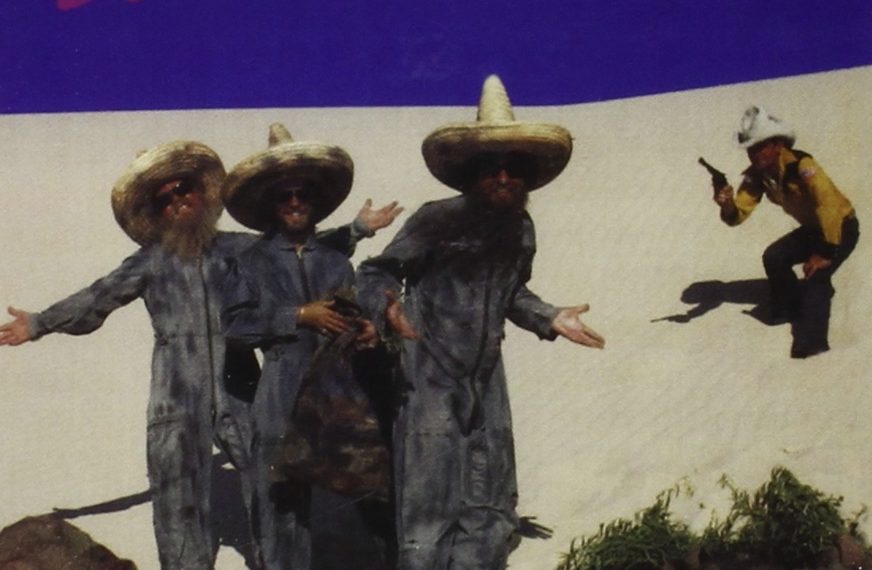 Auf dem Albumcover "El Loco" von ZZ Top sieht man drei Männer mit Hüten in der Wüste. Im Hintergrund steht ein Mann mit Pistole.