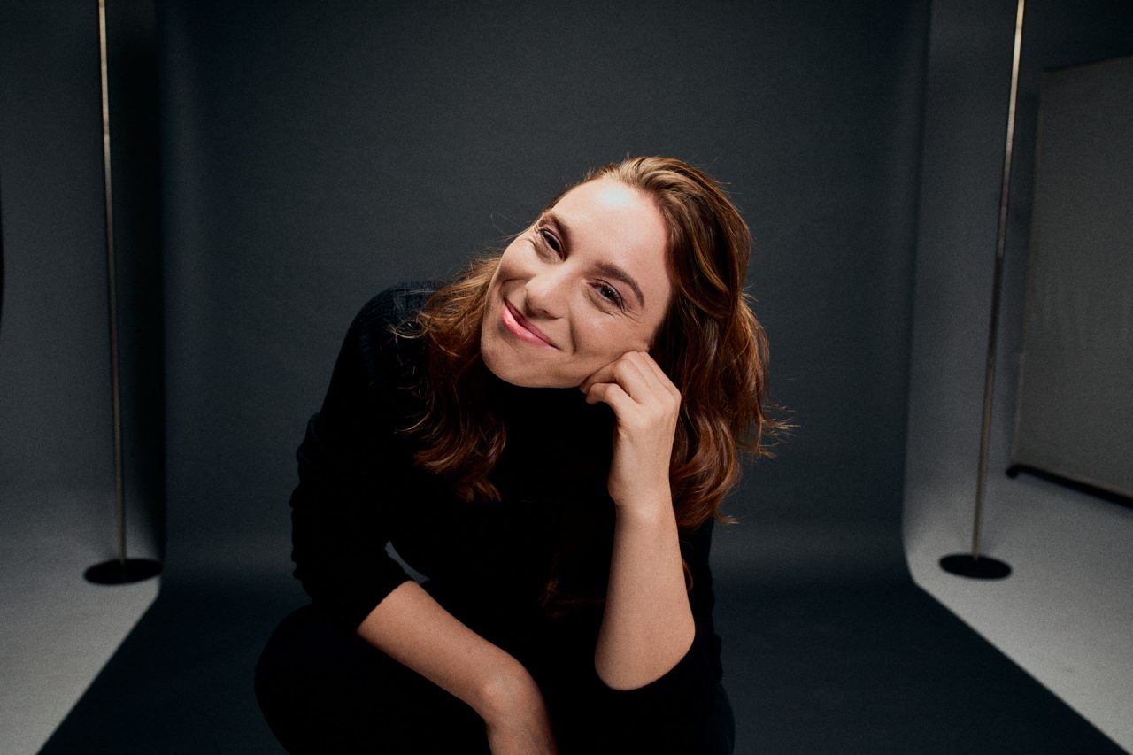 Luisa Filip sitzt in einem Fotostudio vor einer grauen Wand und lächelt in die Kamera.