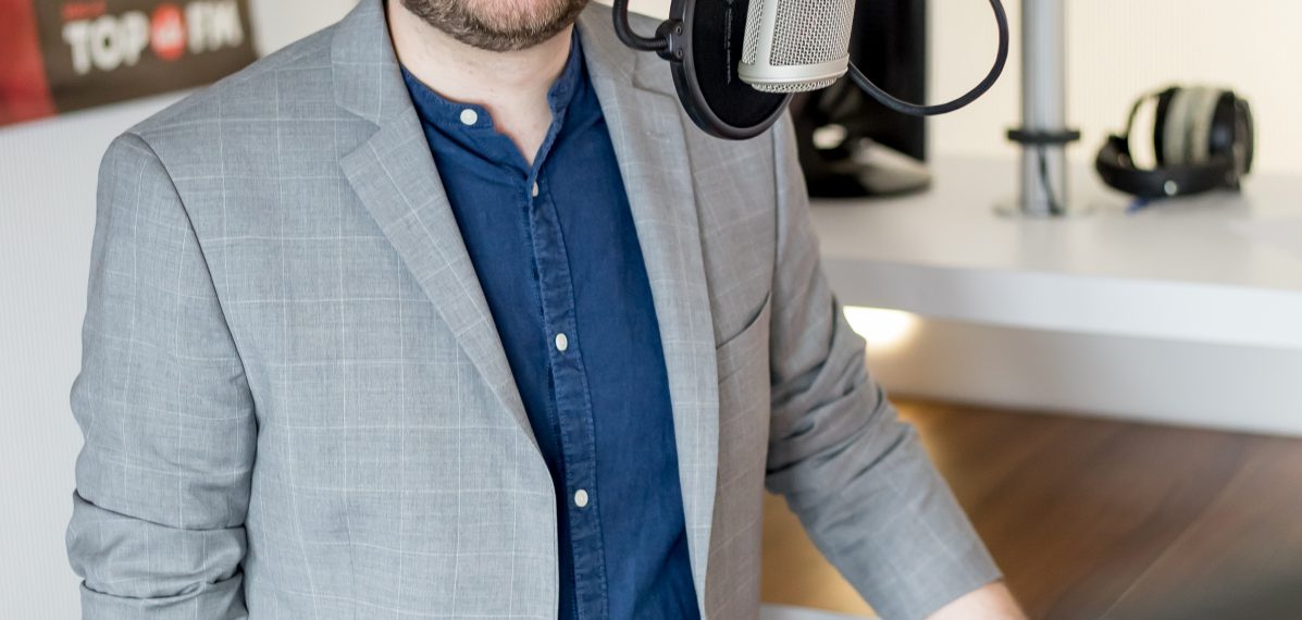 Maxi Auer steht im Studio von Radio TOP FM am Mischpult vor dem Mikrofon.