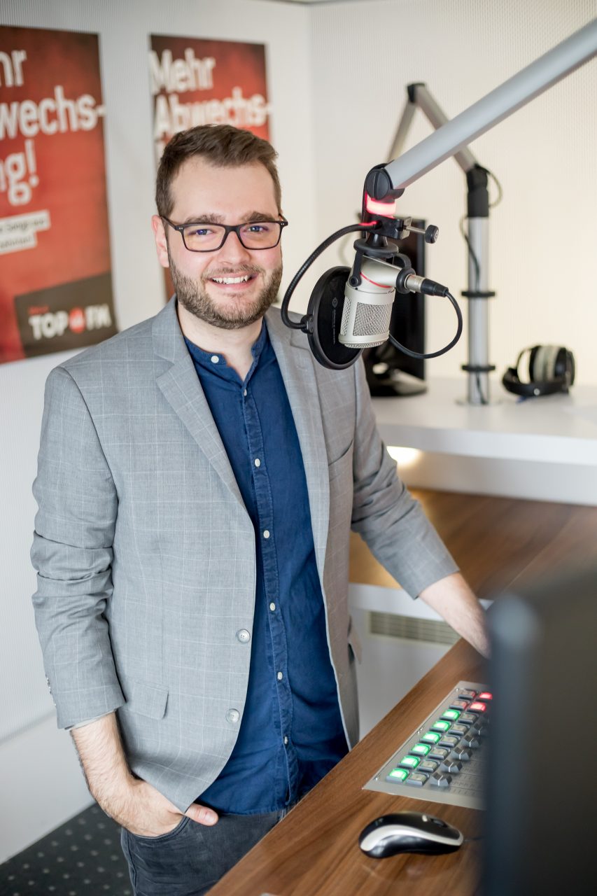 Maxi Auer steht im Studio von Radio TOP FM am Mischpult vor dem Mikrofon.