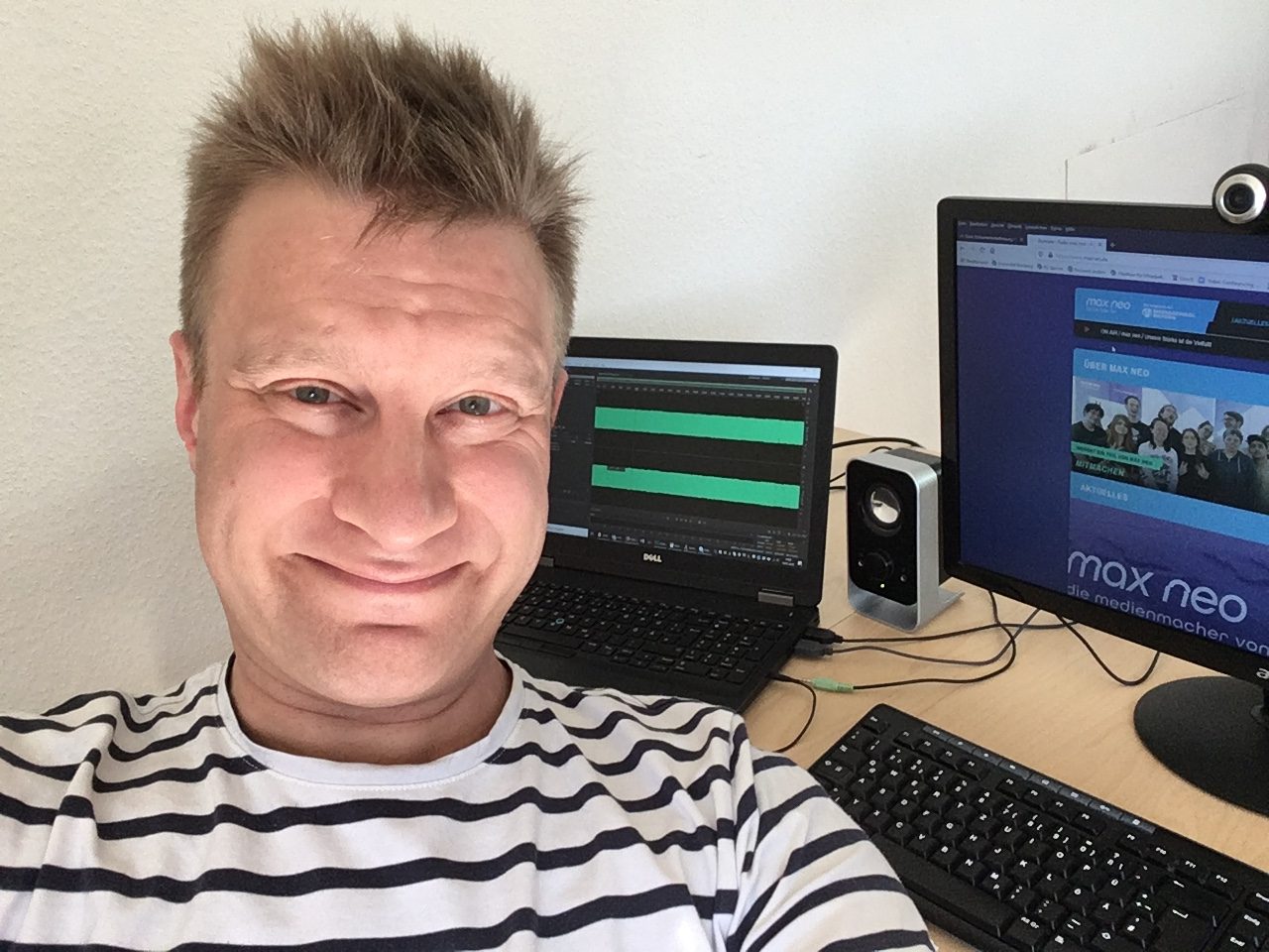 Holger Müller sitzt an seinem Schreibtisch im Home Office. Im Hintergrund des Selfies sind ein PC mit Tastatur und ein Laptop zu sehen.