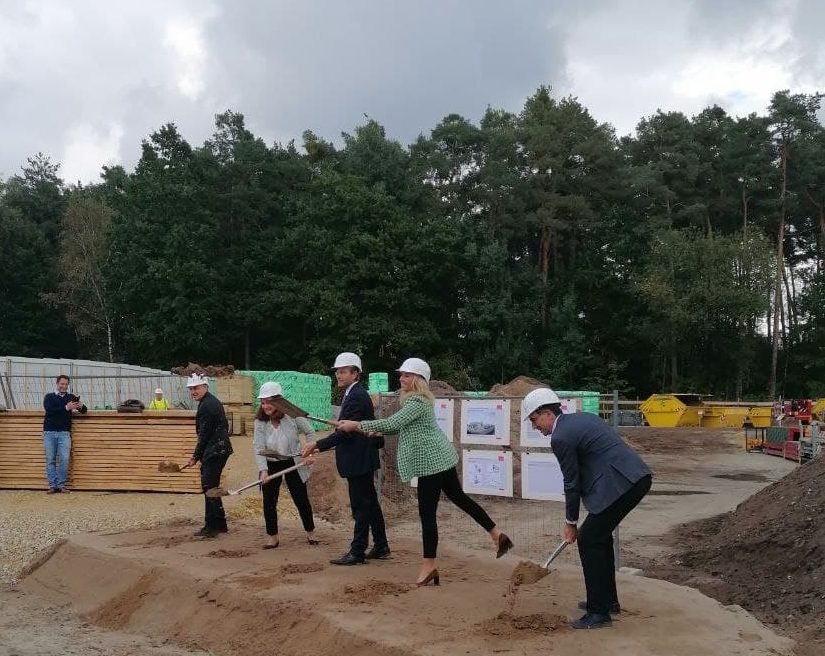 Auf dem Foto sind fünf Menschen zu sehen, die Schaufeln mit Erde in die Luft werfen, um einen symbolischen Spatenstich zu machen.