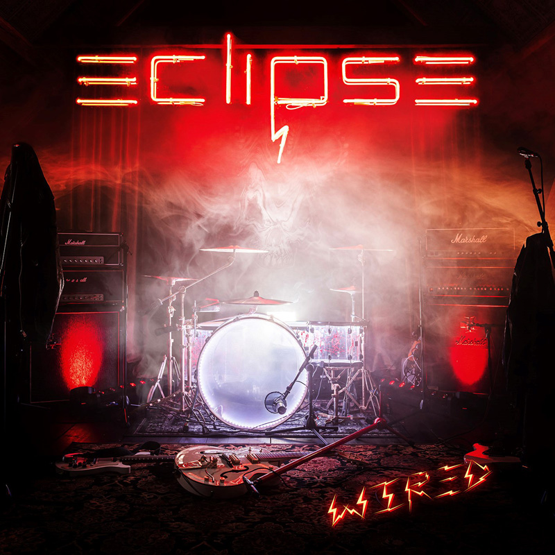 Das Albumcover "Wired" von Eclipse zeigt einen dunklen Raum, in dem ein Schlagzeug, eine Gitarre, ein Mikrofonständer und vieles mehr stehen. Darüber wabern Nebelschwaden und es hängt eine Leuchtschrift mit dem Wort "Eclipse".