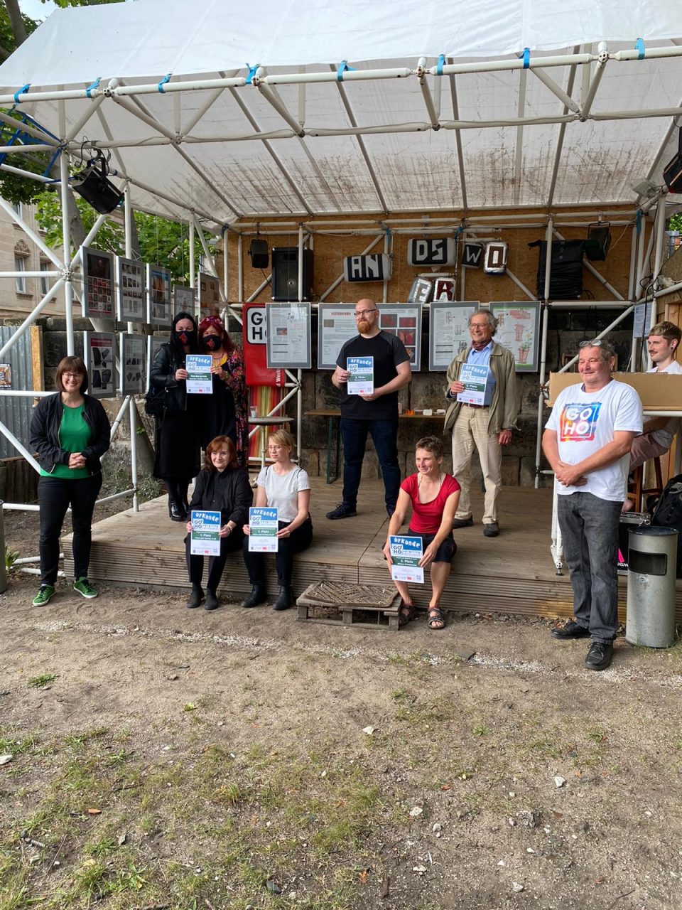 Das Foto zeigt eine Preisverleihung. Es ist ein Gruppenfoto, auf dem zehn Menschen stehen oder sitzen und eine Urkunde in der Hand halten. Im Hintergrund ist eine Bühne zu sehen.