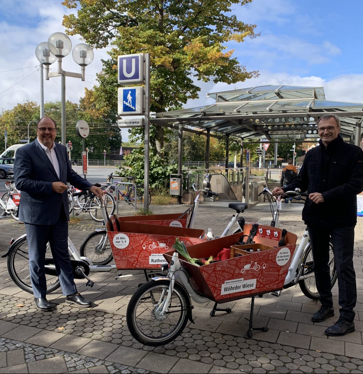 Im Hintergrund ist die U-Bahnstation Wöhrder Wiese zu sehen. Davor stehen Christian Vogel und Josef Hasler. Dazwischen stehen drei Lastenräder der VAG Nürnberg.