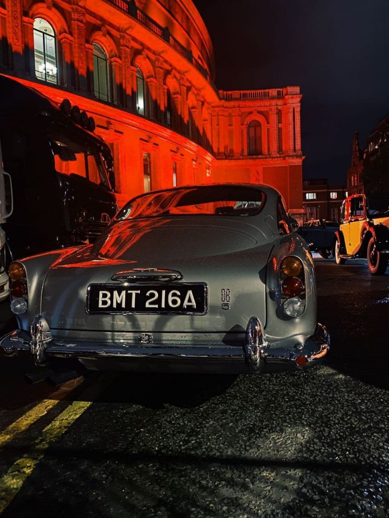 Ein Oldtimer Auto steht vor der rot beleuchteten Royal Albert Hall.