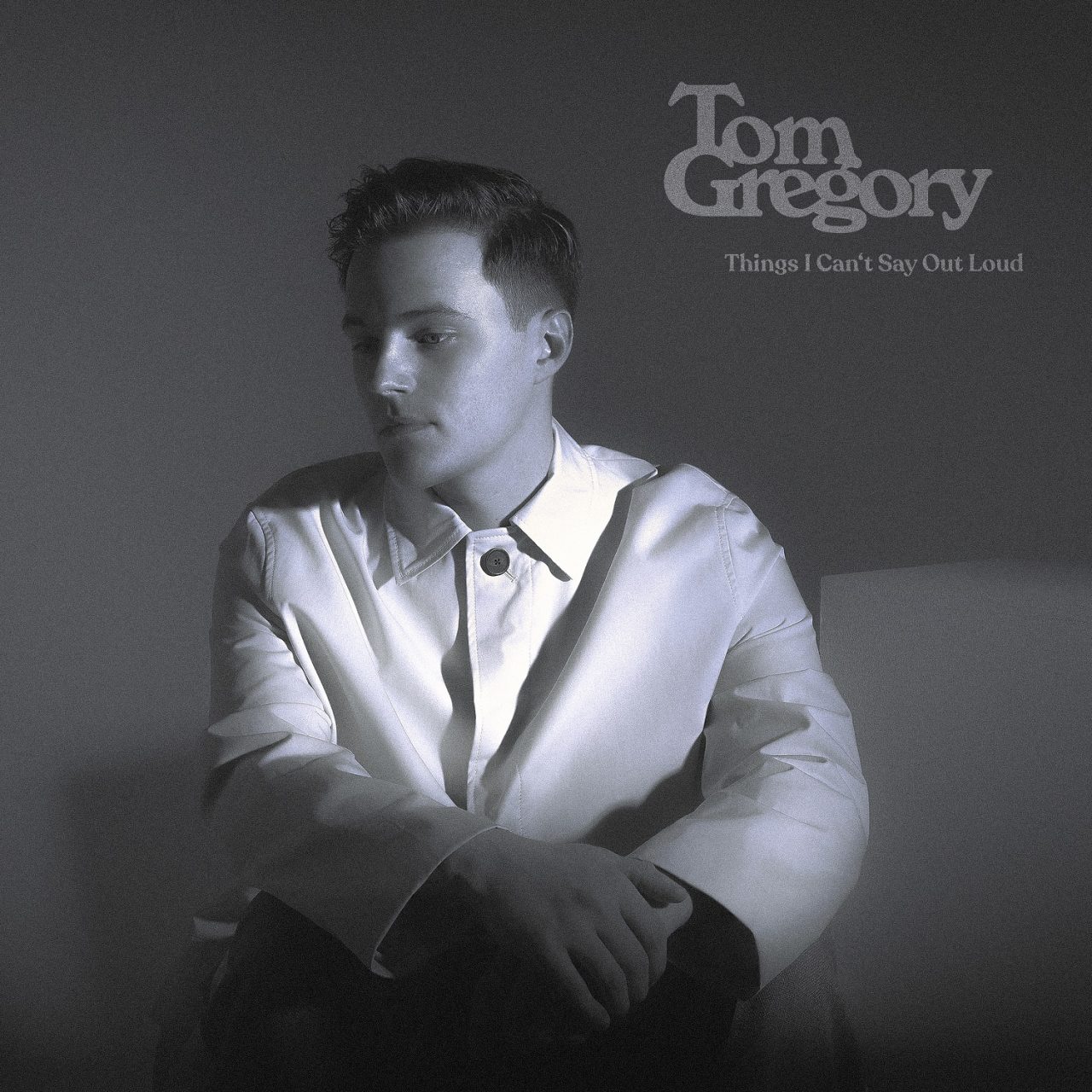 Das Albumcover "Things I Can't Say Out Loud" von Tom Gregory ist schwarz-weiß. Es zeigt den Musiker, wie er da sitzt und nachdenklich in die Ferne schaut.