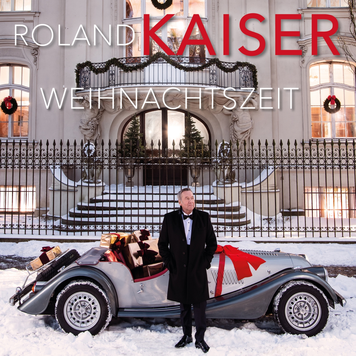 Das Albumcover "Weihnachtszeit" von Roland Kaiser zeigt den Musiker vor einem geschmückten und mit Geschenken beladenen Oldtimer, der vor einer ebenfalls geschmückten, herrschaftlichen Villa parkt.