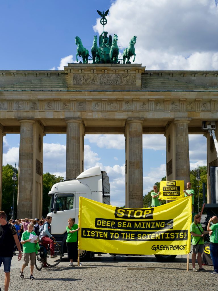 Greenpeace-Aktivist*innen protestieren vor dem Brandenburger Tor in Berlin. Auf dem Plakat steht "Stop Deep Sea Mining - listen to the scientists!"