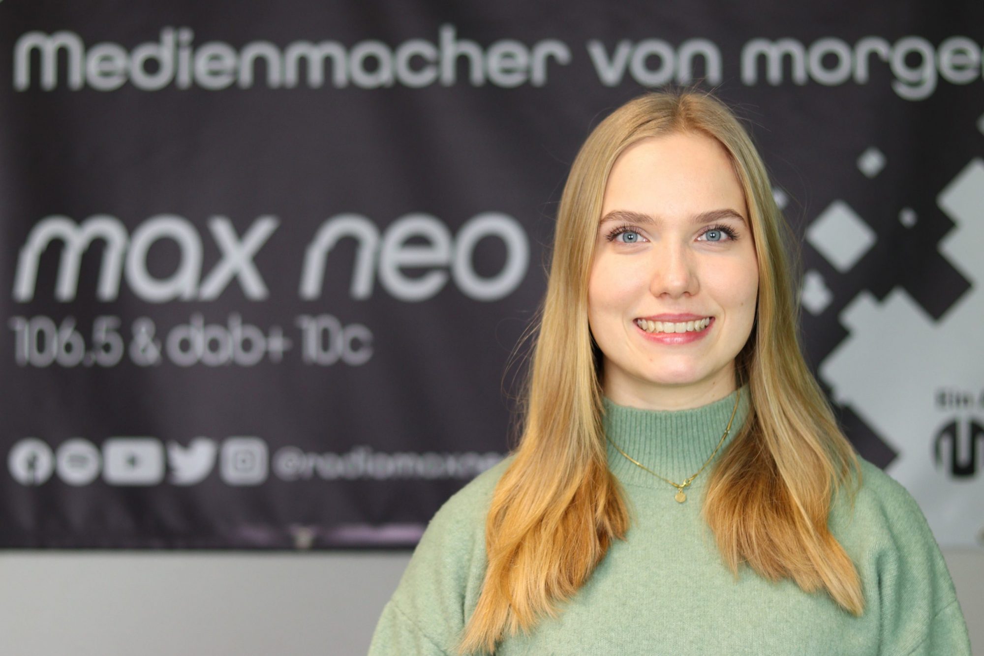 Auf dem Foto ist Praktikantin Leoni Schaber im Porträt zu sehen, die vor dem max neo Banner steht.