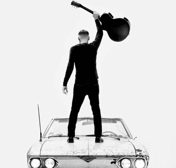 Das Albumcover "So Happy It Hurts" von Bryan Adams zeigt den Sänger von hinten, wie er auf einem Oldtimer steht und eine Gitarre in der Hand hält. Das Foto ist schwarz-weiß.