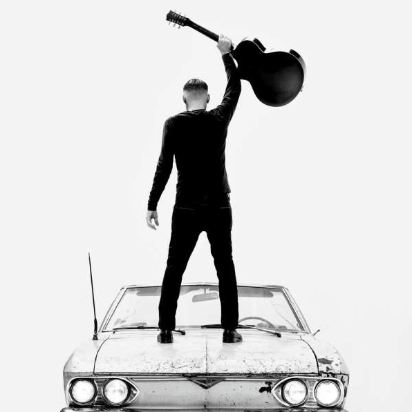 Das Albumcover "So Happy It Hurts" von Bryan Adams zeigt den Sänger von hinten, wie er auf einem Oldtimer steht und eine Gitarre in der Hand hält. Das Foto ist schwarz-weiß.