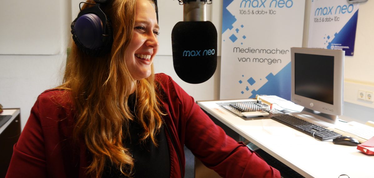Pauline Gwosdz sitzt lachend vor einem max neo-Mikrofon im Studio.