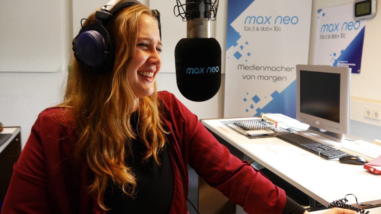 Pauline Gwosdz sitzt lachend vor einem max neo-Mikrofon im Studio.