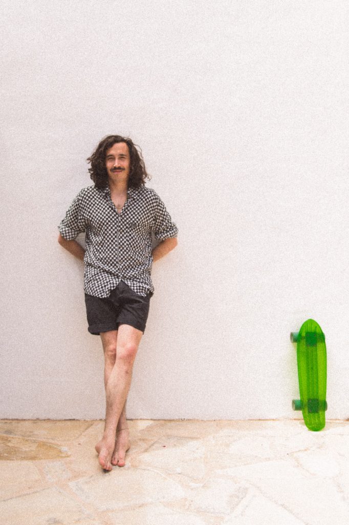 Frinc lehnt an einer weißen Wand, neben ihm steht ein grünes Skateboard.