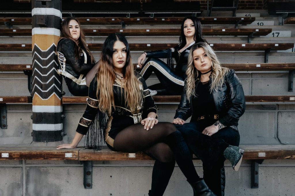 Das Foto zeigt die vier Frauen von Thundermother, die auf einer Tribüne sitzen und in die Kamera schauen.