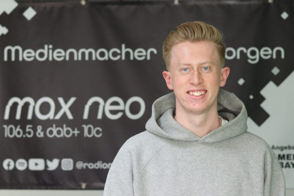 Das Foto zeigt den Praktikanten Tobias Bedau im Porträt vor dem max neo Banner.