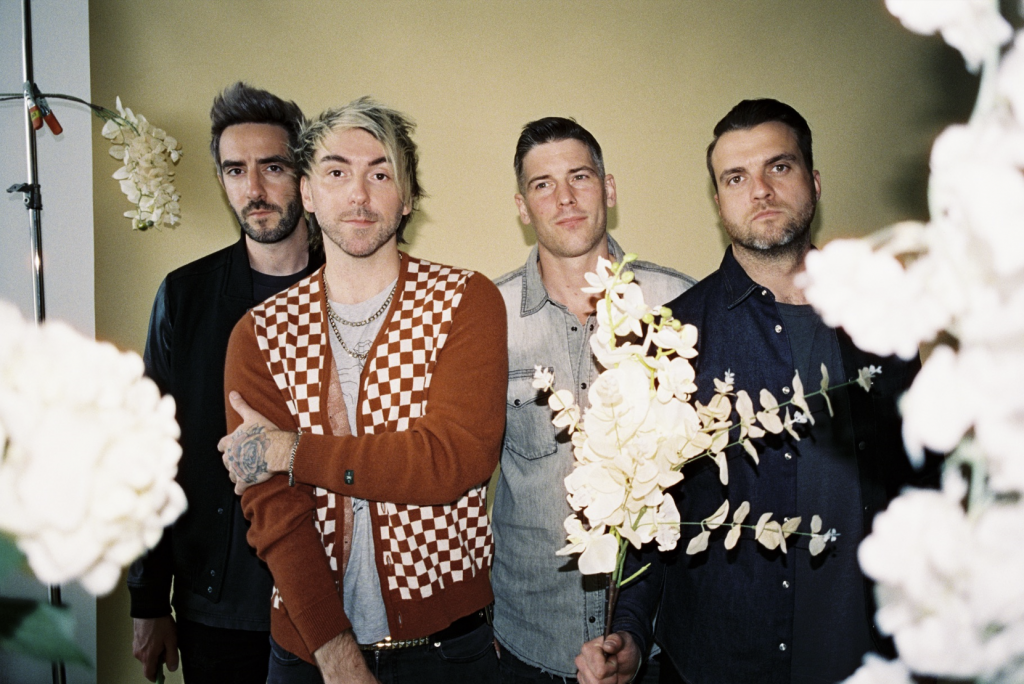 Das Foto ist ein Gruppenbild der Band All Time Low. Es zeigt die vier Jungs, die vor der Kamera posieren.