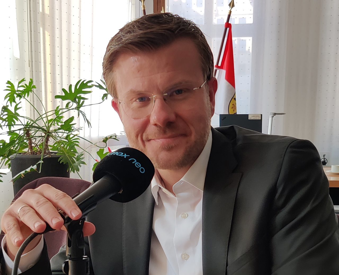 Das Foto zeigt Nürnbergs Oberbürgermeister Marcus König, wie er vor einem Mikrofon am Tisch seines Büros sitzt.