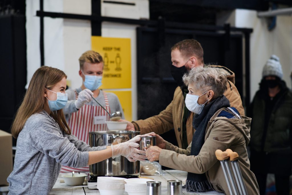 Das Foto zeigt eine Helferin, die Suppe an Bedürftige und Obdachlose verteilt.