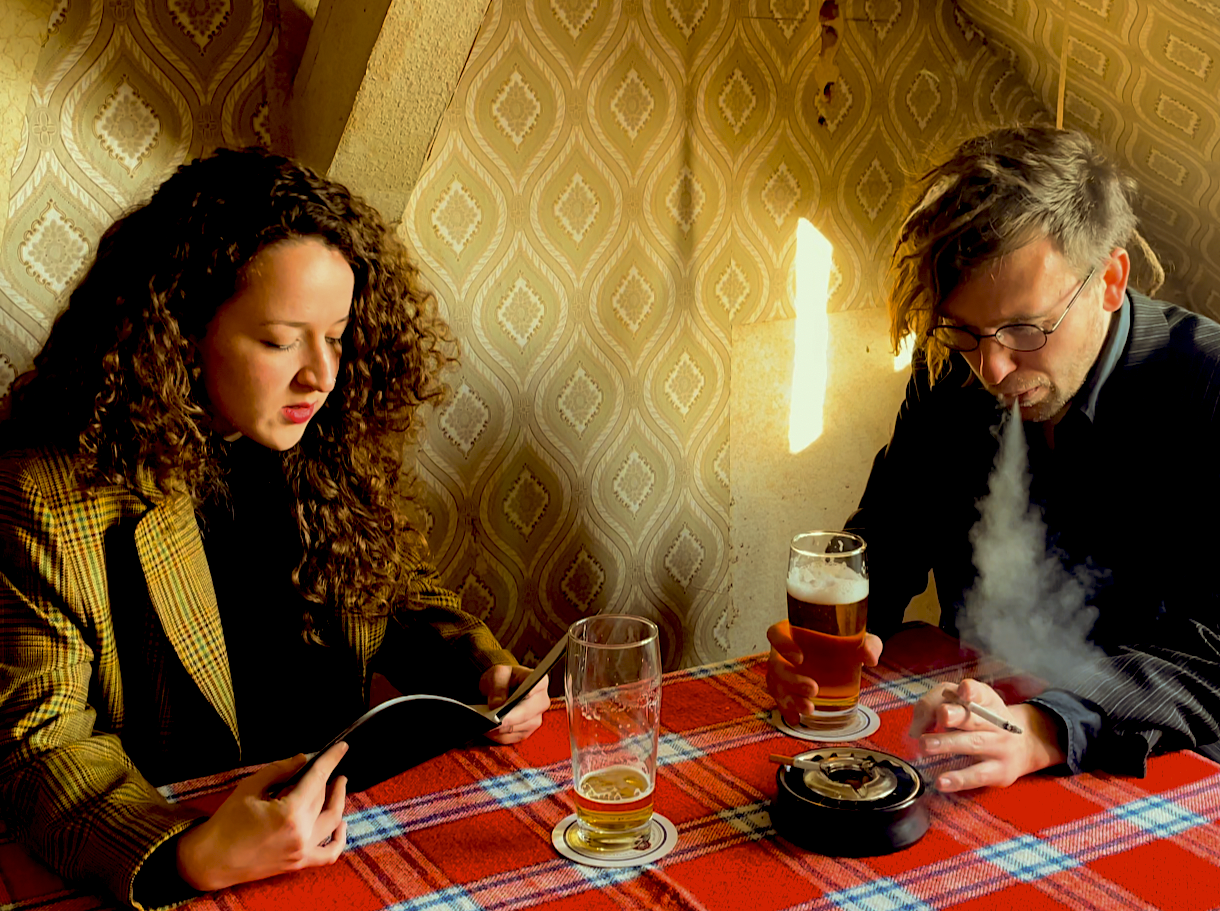 Das Foto zeigt die zwei Bandmitglieder von "Nun flog Dr. Bert Rabe", wie sie an einem Tisch sitzen, Bier trinken und rauchen.