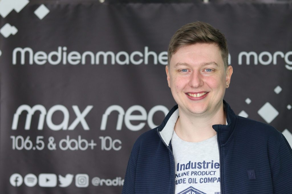 Das Foto zeigt Moritz Bayer im Porträt vor dem max neo Banner.