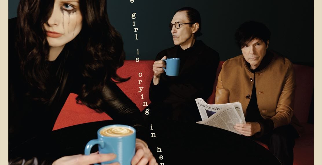 Das Albumcover "The Girl Is Crying In Her Latte" von Sparks zeigt eine Frau im Vordergrund, die einen Kaffee in der Hand hält und weint. Im Hintergrund sitzen die zwei Bandmitglieder mit einer Tasse und einer Zeitung auf einem Sofa.