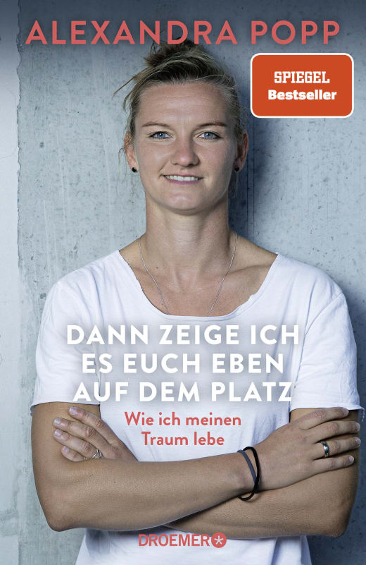 Das Buchcover "Dann zeige ich es euch eben auf dem Platz" zeigt die Fußballerin Alexandra Popp im Porträt mit verschränkten Armen.