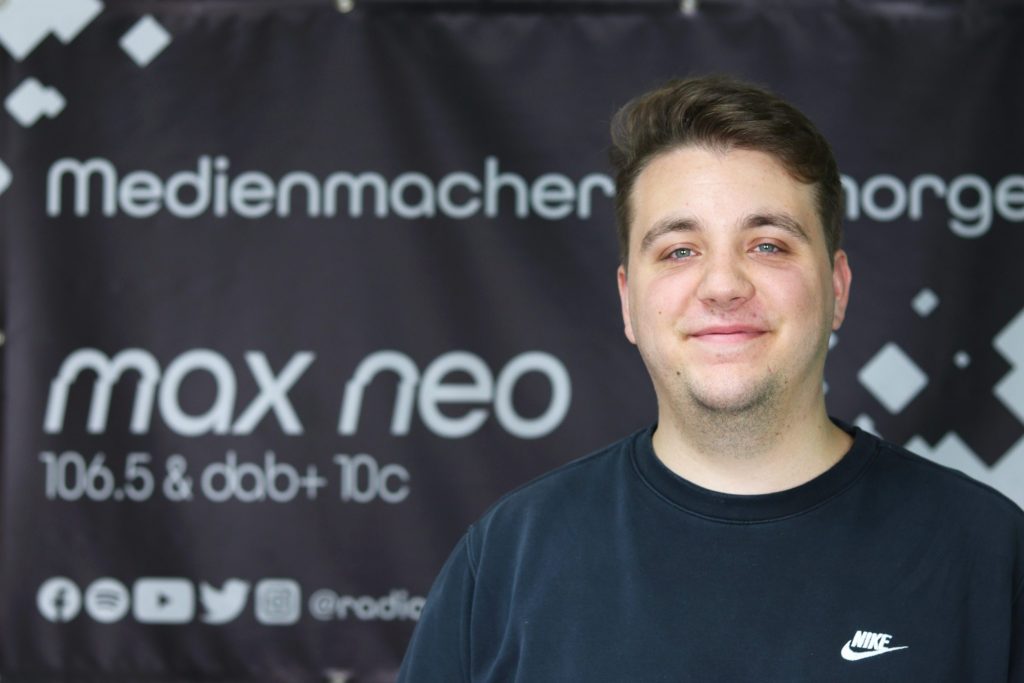 Auf dem Foto ist Julian Pilz im Porträt vor dem max neo Banner zu sehen.