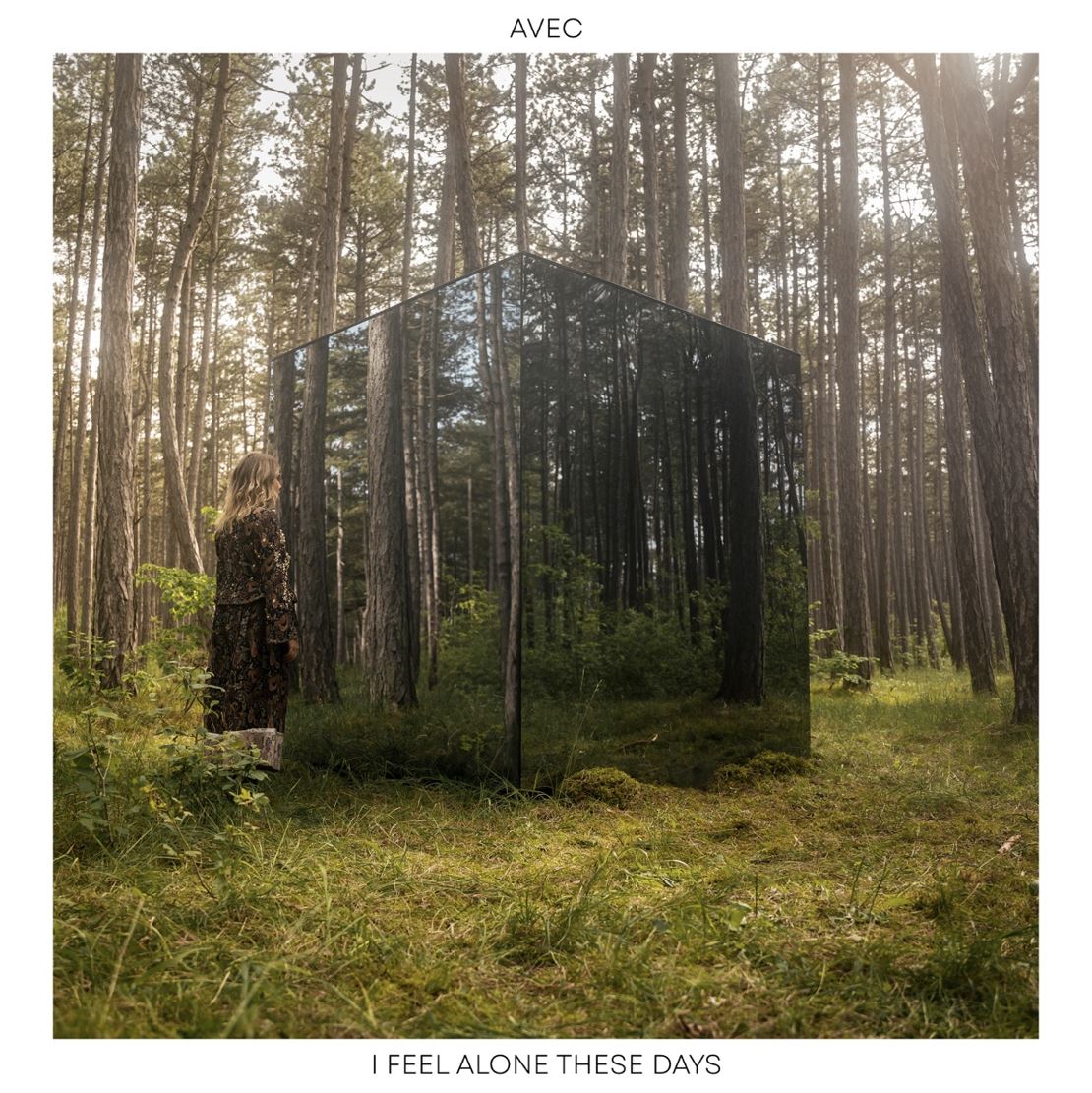 Das Albumcover "I Feel Alone These Days" von Avec zeigt die Musikerin in einem Wald. Sie steht vor einem großen, verspiegelten Würfel.