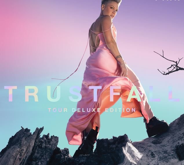 Das Albumcover "Trustfall (Tour Deluxe Edition)" von P!nk zeigt die Sängerin von hinten, wie sie auf einem Baumstamm steht und über die Schulter zur Kamera schaut.