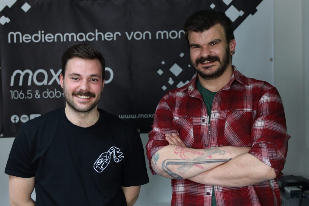 Das Foto zeigt zwei Mitglieder der Nürnberger/Fürther Band CLSTRFCK vor dem max neo Banner.