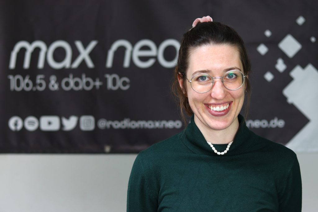 Auf dem Foto ist Riccarda Rascher im Porträt vor dem max neo Banner zu sehen.