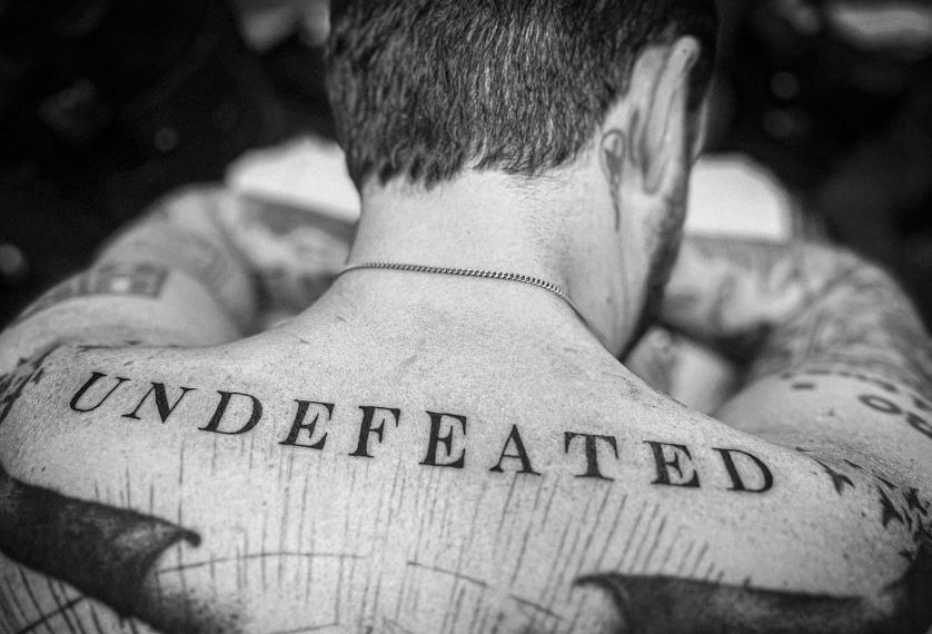 Das Albumcover "Undefeated" von Frank Turner zeigt den Musiker von hinten in schwarz-weiß. Unterhalb seines Nackens ist ein Tattoo mit dem Schriftzug "Undefeated", der zugleich der Albumname ist.