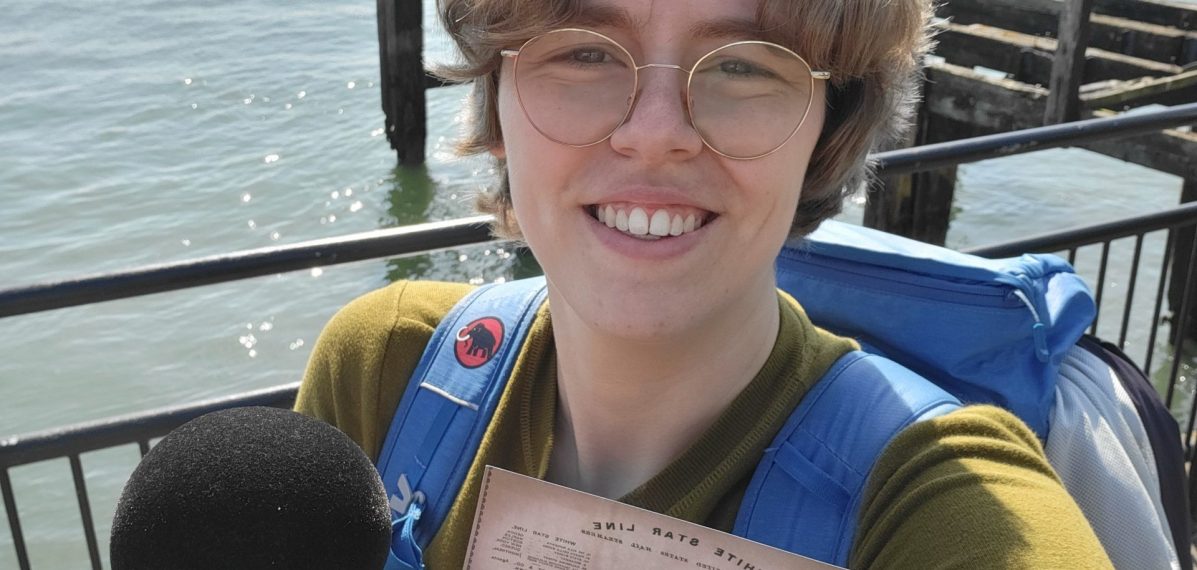 Das Foto zeigt Lena Schnelle mit Mikrofon und Fahrkarte in der Hand vor dem Meer.