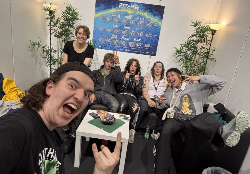 Das Foto ist ein Selfie von den Moderator*innen Silas und Lena mit der Band Leftovers.