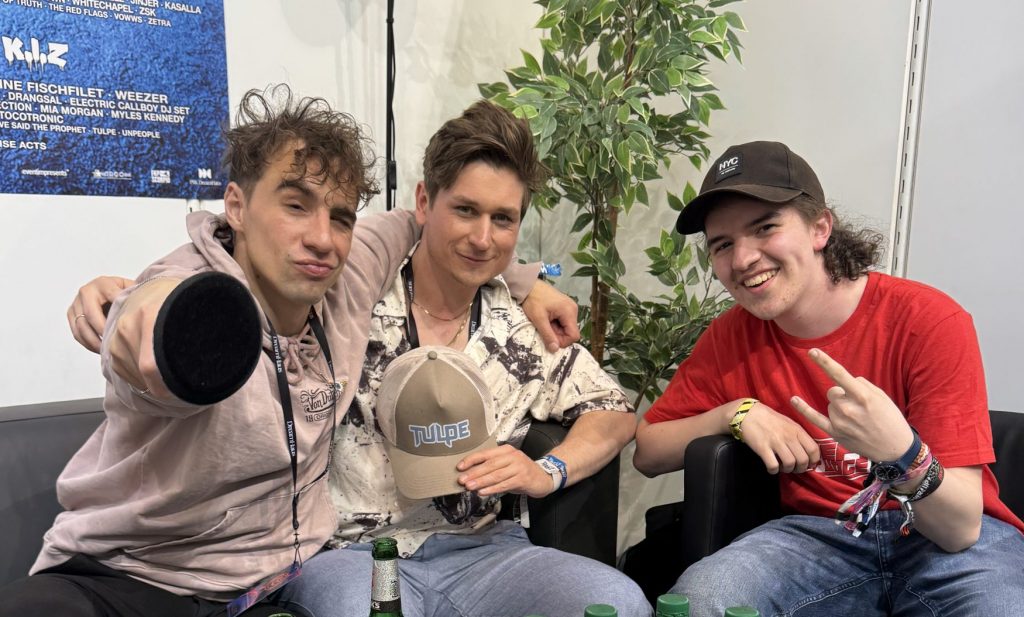 Das Foto zeigt Moderator Silas mit zwei Bandmitgliedern von Tulpe.