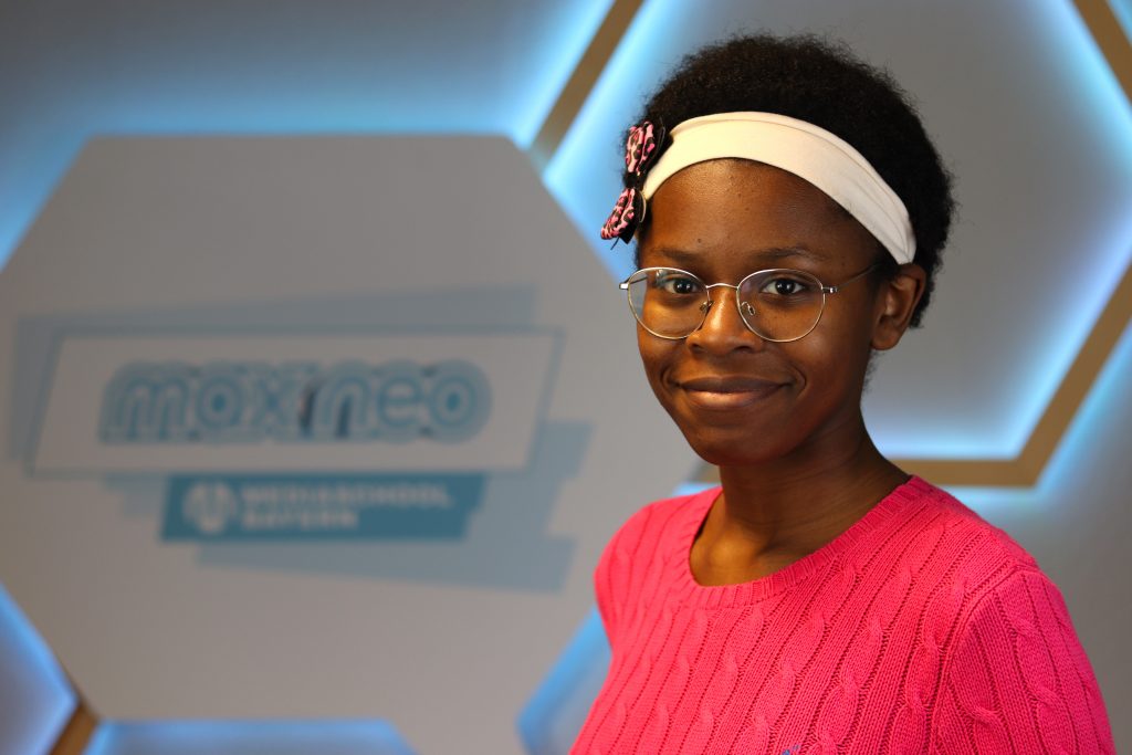 Das Foto zeigt Chanecia Fayola Monteu Kouemou im Porträt vor dem max neo Logo.