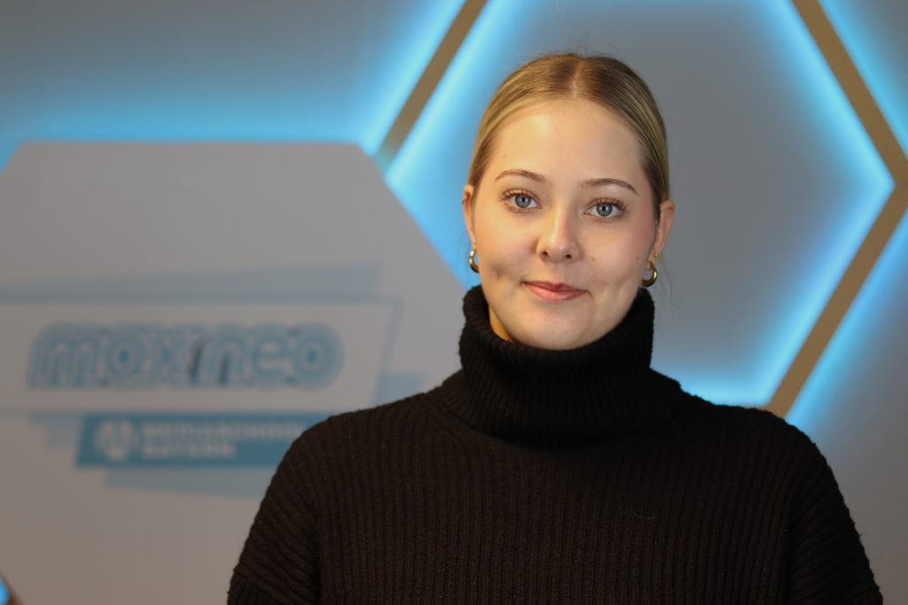 Das Foto zeigt Praktikantin Veronika Gaus im Porträt vor dem max neo Schild.