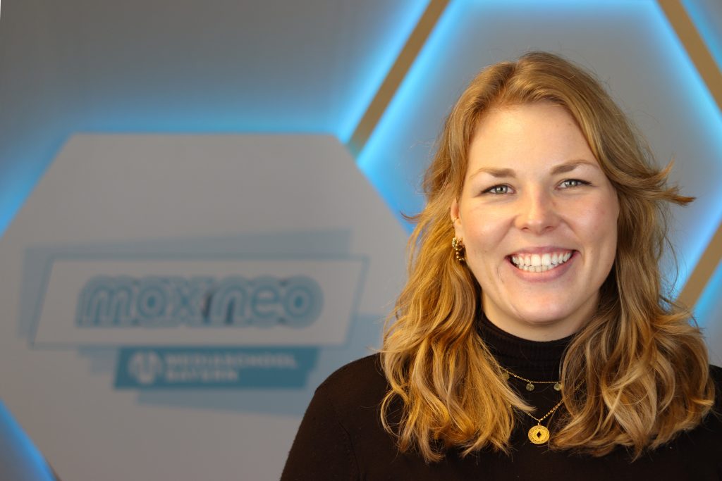 Das Foto zeigt Lilly Fröbel im Porträt vor dem max neo Logo.