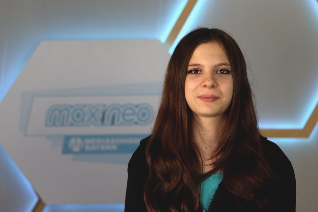 Das Foto zeigt die Praktikantin Rosa Braun vor dem max neo Banner.